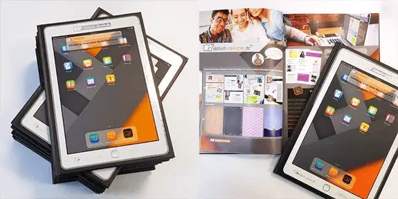 Gedrucktes Abibuch-Muster in Tablet-Optik, gestapelt und neben einem aufgeschlagenen Musterbuch, das Design-Optionen zeigt.